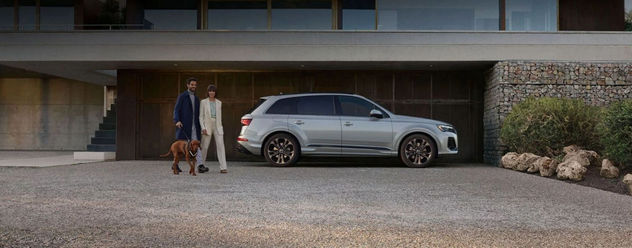 Couple and a dog walking next to a silver 2025 Audi Q7.